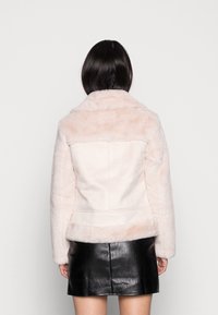 Faux furjacka i ljusrosa med en mjuk textur, med en bred krage och en figursydd design, kompletterad med en enkel baksida.