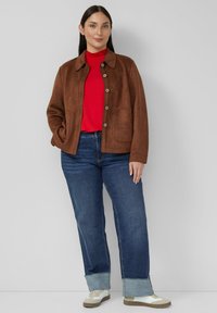 Brązowa zamszowa kurtka zapinana na guziki, z dużymi kieszeniami, noszona na czerwonym golfie. W połączeniu z niebieskimi dżinsami i beżowo-białymi sneakersami.