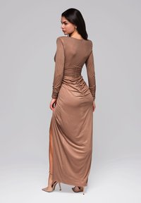 Abito lungo marrone a maniche lunghe con silhouette aderente, tessuto arricciato in vita e apertura laterale, realizzato in un tessuto liscio e lucido.