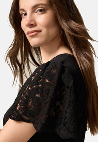 Black top featuring intricate lace puff sleeves with floral patterns. Smooth fabric on the body, showcasing a fitted design.
