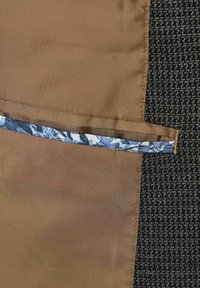 Brauner Stoff mit einer glatten Textur zeigt einen gemusterten Akzentstreifen in Blau- und Weißtönen, vor einem dunklen, strukturierten Hintergrund.