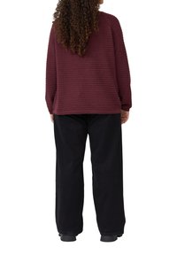 Maroonschwarzer gerippter Pullover mit langen Ärmeln, lockerer Schnitt, kombiniert mit weit geschnittenen schwarzen Hosen. Die Textur ist in den horizontalen Streifen des Pullovers sichtbar.