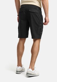 Shorts cargo noirs avec une coupe décontractée, en tissu coton. Dotés de poches latérales et d'une taille lisse et plate. Portés avec des baskets légères.