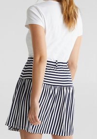 Jupe à rayures avec une ceinture ajustée et un ourlet évasé, présentant des rayures verticales bleu marine et blanches ; portée avec un t-shirt blanc uni.