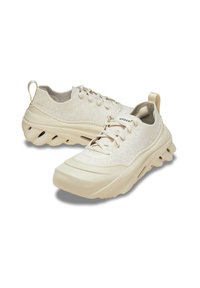Beige Sneaker mit strukturiertem Obermaterial, auffälliger Sohle mit Luftkanälen und einer Zuglasche an der Ferse für einfaches Anziehen. Verfügt über Schnürsenkel und Logo.