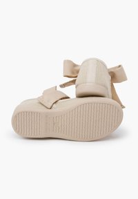 Scarpe in tela beige con tomaia testurizzata e grandi fiocchi di tessuto su ciascun lato. Le suole in gomma presentano un motivo a tassello ondulato per garantire aderenza.