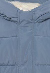 Ljusblått puffer-jacka med en mjuk vit foder, med mjukt yttermaterial, huva och dragkedjestängning. Kviltad struktur med horisontella sömmar.