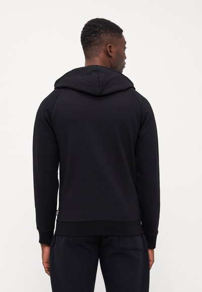 Black cotton hoodie with a drawstring hood, raglan sleeves, ribbed cuffs, and hem. Features a subtle label accent near the hem.