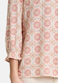Top leggero con motivo floreale in colori pastello, maniche lunghe e polsini arricciati. Presenta intricati disegni circolari in tutto il capo.
