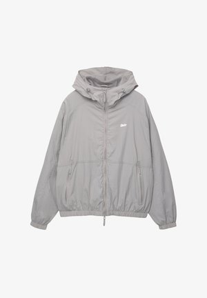 Helle graue Windjacke mit Kapuze, Reißverschluss vorne und zwei Seitentaschen. Verfügt über elastische Bündchen und ein dezentes Logo auf der Brust.