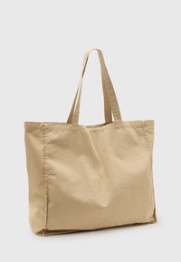 Beige Baumwolltasche mit zwei langen Trägern, rechteckiger Form, weicher Textur und sichtbaren Nähten. Ideal für den täglichen Gebrauch.