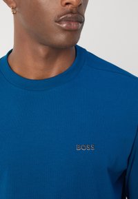 Blå bomulls T-skjorte med rund hals som har en liten sølvfarget "BOSS"-logo på brystet, ribbet halslinning og glatt tekstur.