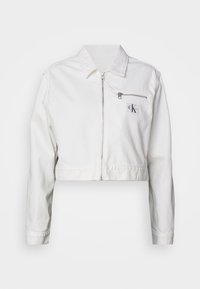 Giacca cropped bianca in misto cotone, caratterizzata da maniche lunghe, una chiusura anteriore con zip e una tasca sul petto sinistro con dettaglio del logo. Finitura testurizzata.
