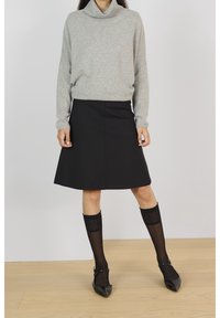Maglione grigio a collo alto, gonna nera a campana, calze nere a fantasie fino al ginocchio e ballerine nere a punta. Design semplice e versatile con texture morbide.