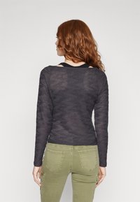 Svart, texturerad långärmad topp med ribbat mönster. Bärs med olivgröna byxor som har fickor och en tapered passform.