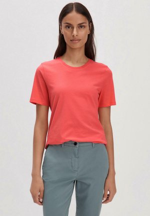 T-shirt corail à manches courtes en coton lisse, avec un col rond et une coupe décontractée, associé à un pantalon vert clair.