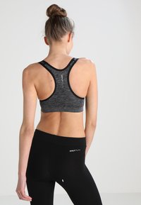 Grafitszürke sportmelltartó racerback kialakítással és fekete díszítéssel, textúrált anyagból. Fekete leggings sima felülettel. Mindkettőn logók találhatók.