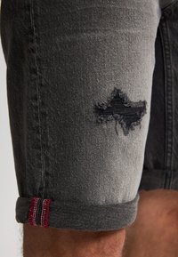 Zwarte denimshorts met een versleten stuk op de dij, met omgeslagen zoom en contrasterende rode en witte stiksels.