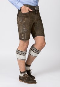 Shorts en cuir marron avec des coutures décoratives, des poches et des boutons. Assortis à des chaussettes en maille jusqu'aux genoux et des chaussures marron.