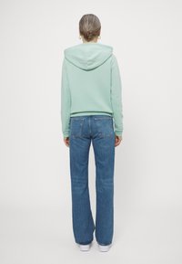 Mint green hooded sweatshirt with ribbed cuffs, paired with high-waisted blue jeans. The outfit is casual and fitted for comfort.
