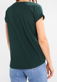 Mörkgrön t-shirt med korta ärmar och rullade manschetter, tillverkad av mjuk bomull. Har en rund halsringning och en avslappnad passform med rak nederkant.