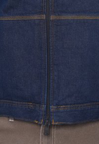 Τζιν μπουφάν με σκούρο μπλε φινίρισμα, με ραφές αντίθεσης σε πορτοκαλί, κλείσιμο με φερμουάρ και δομημένο σχέδιο.