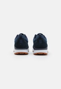 Granatowe buty sportowe z zamszową cholewką, kontrastującą białą podeszwą środkową i brązową gumową podeszwą. Posiadają wyściełane kołnierze i pętelki.