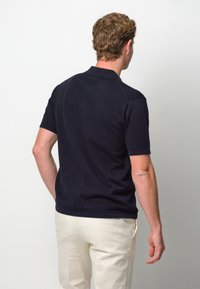 Polo shirt di un blu navy scuro con tessuto a maglia testurizzato e maniche corte, dotato di un colletto classico. Abbinato a pantaloni di colore chiaro.