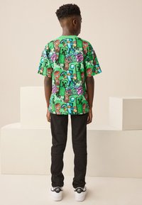 Groen shirt met korte mouwen en grafische prints van spelelementen, gecombineerd met zwarte broek en witte sneakers. Heeft een ontspannen pasvorm en levendige kleuren.