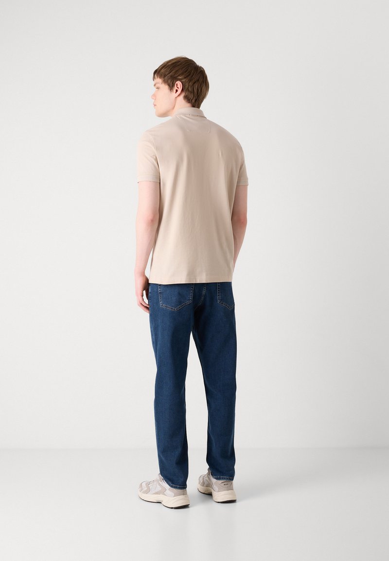 Polo-shirt beige à manches courtes, tissu lisse ; associé à un jean bleu foncé, coupe décontractée ; baskets claires avec des accents de design subtils.