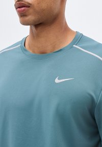 Κοντινό πλάνο ατόμου που φορά μπλε αθλητική μπλούζα Nike με λευκό λογότυπο και λευκές λεπτομέρειες στους ώμους.