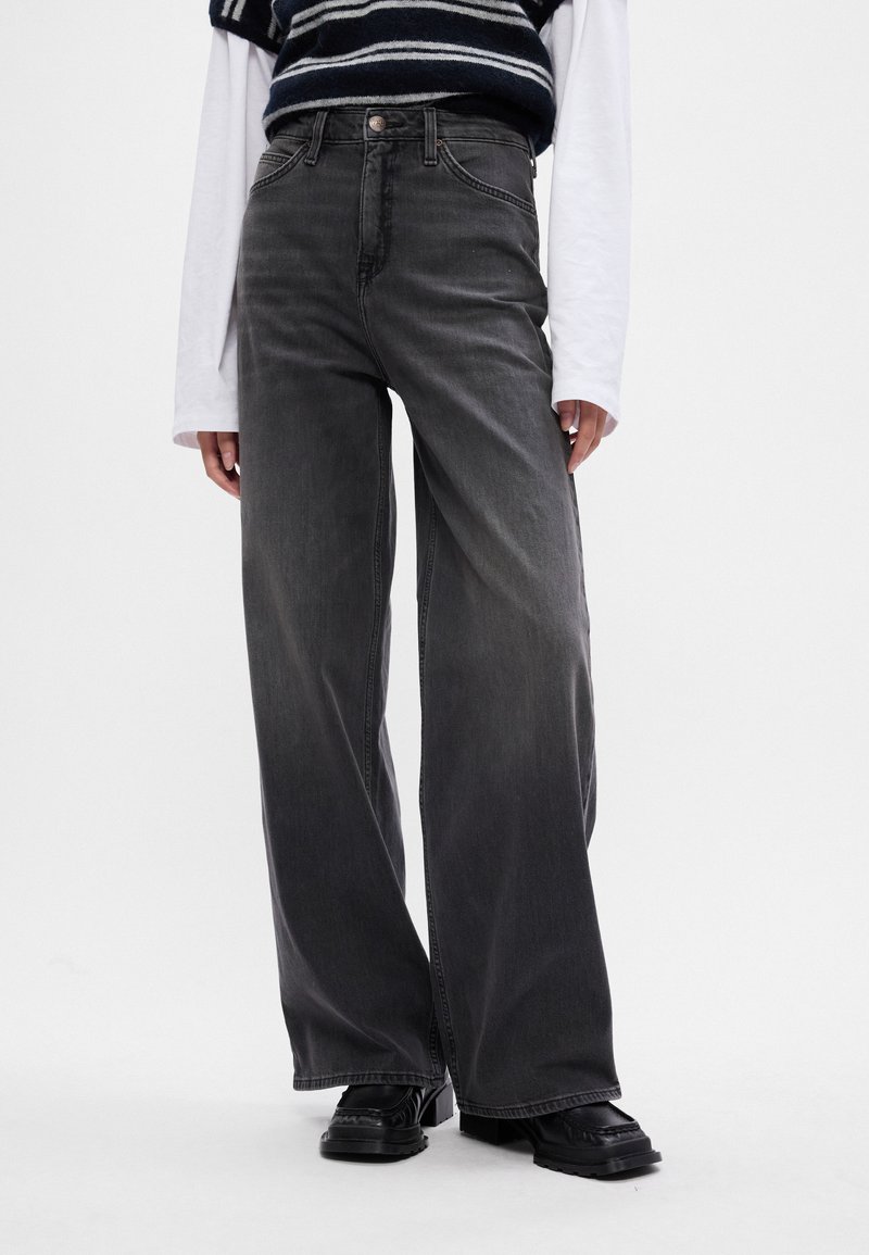 Szerokie czarne dżinsy typu mom z wyblakłym wykończeniem, wysokim stanem, pięcioma kieszeniami oraz kontrastowymi przeszyciami.