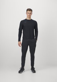 Top sportiv negru cu mânecă lungă și pantaloni asortați. Material neted cu un design ajustat, evidențiat de un mic logo pe piept și pe lateral.
