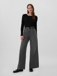 Jean large gris en denim, avec une taille haute et des passants de ceinture, associé à un haut noir ajusté à manches longues et des mocassins noirs.