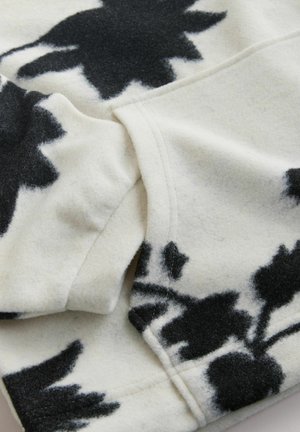 Vilnonė audinio medžiaga su gėlių raštu, spalvų kreminė ir juoda. Audinys pasižymi minkšta tekstūra, matomomis siūlėmis ir švelniu kritimu. Dizainą sudaro didelės, abstrakčios gėlės.