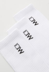 Valged tekstureeritud spord socksid, millel on musta logo tikand. Kolm paari on näidatud, rõhutades ribakujundust ja ühtlast mustrit.