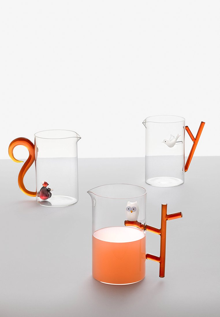 Trzy przezroczyste dzbanki z kolorowymi akcentami: jeden z uchwytem w kształcie wiewiórki, drugi z ptasim detalem, a trzeci z sową i pomarańczowym dnem.