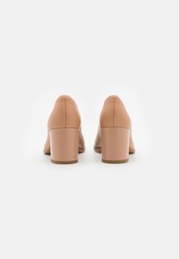 Chaussures à talons blocs en cuir nude avec une texture lisse et un bout arrondi, dotées d'un talon de hauteur moyenne et d'un design minimaliste.