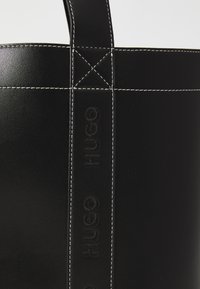 Svart läderhandväska med kontrasterande vit sömnad, som har ett präglat varumärke och en snygg, rektangulär design.