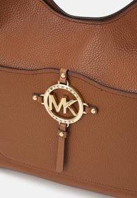 Sac à main en cuir marron texturé avec emblème logo MK Michael Kors doré et détail décoratif sur la bandoulière.