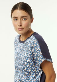 Blau gemustertes T-Shirt mit weißen geometrischen Designs, ausgestattet mit navyblauen Raglanärmeln und glatter Stoffstruktur.