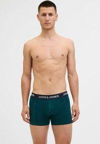 Grüne Baumwoll-Boxershorts mit einem schwarzen elastischen Bund, der den Markennamen "JACK & JONES" in Weiß trägt, eng am Körper anliegend.