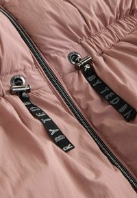 Giacca rosa con zip nera e due lacci neri dotati di fermagli argentati e testo bianco "BY TED BAKER" su ciascun laccio.