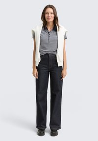 Klassisk stripet polo t-shirt i marineblå og hvid; parret med mørke, brede denimjeans; lagdelt med en cremefarvet ærmeløs sweater.