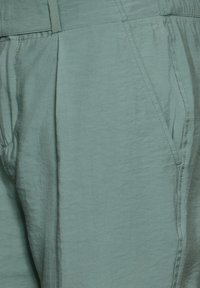 Helles türkisfarbenes Gewebe mit einer weichen, strukturierten Oberfläche. Verfügt über Falten und Seitentaschen und zeigt saubere Nähte sowie eine lockere Silhouette.