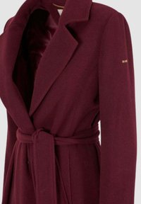 Cappotto in lana bordeaux con colletto a punta, vita con cintura e foderato in satin liscio. Decorato con dettagli dorati sulla manica.