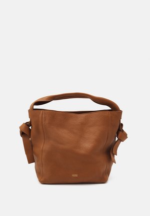 Bolso de cuero marrón con textura suave, asa superior, nudos laterales y un pequeño logo metálico de la marca en el centro frontal.