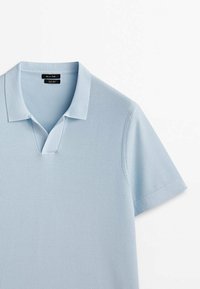 Polo bleu clair à manches courtes avec col et ouverture en V, réalisé en tissu maille texturé, présenté sur fond blanc.