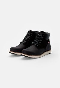 Zwarte enkelboots met een matte afwerking, voorzien van een gevoerde kraag, grijze veters en een lichtgekleurde zool. Inclusief zijaccent en stikseldetails.