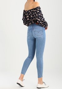 Jeans ajustados de color azul claro, hechos de denim, con una cintura alta y una textura suave. Combinados con una blusa floral fuera del hombro y unas bailarinas en blanco y negro.
